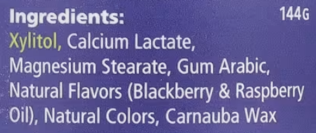 A close-up of a purple ingredients label with white text listing xylitol, calcium lactate, magnesium stearate, gum arabic, natural flavors (blackberry & raspberry oil), natural colors, and carnauba wax.