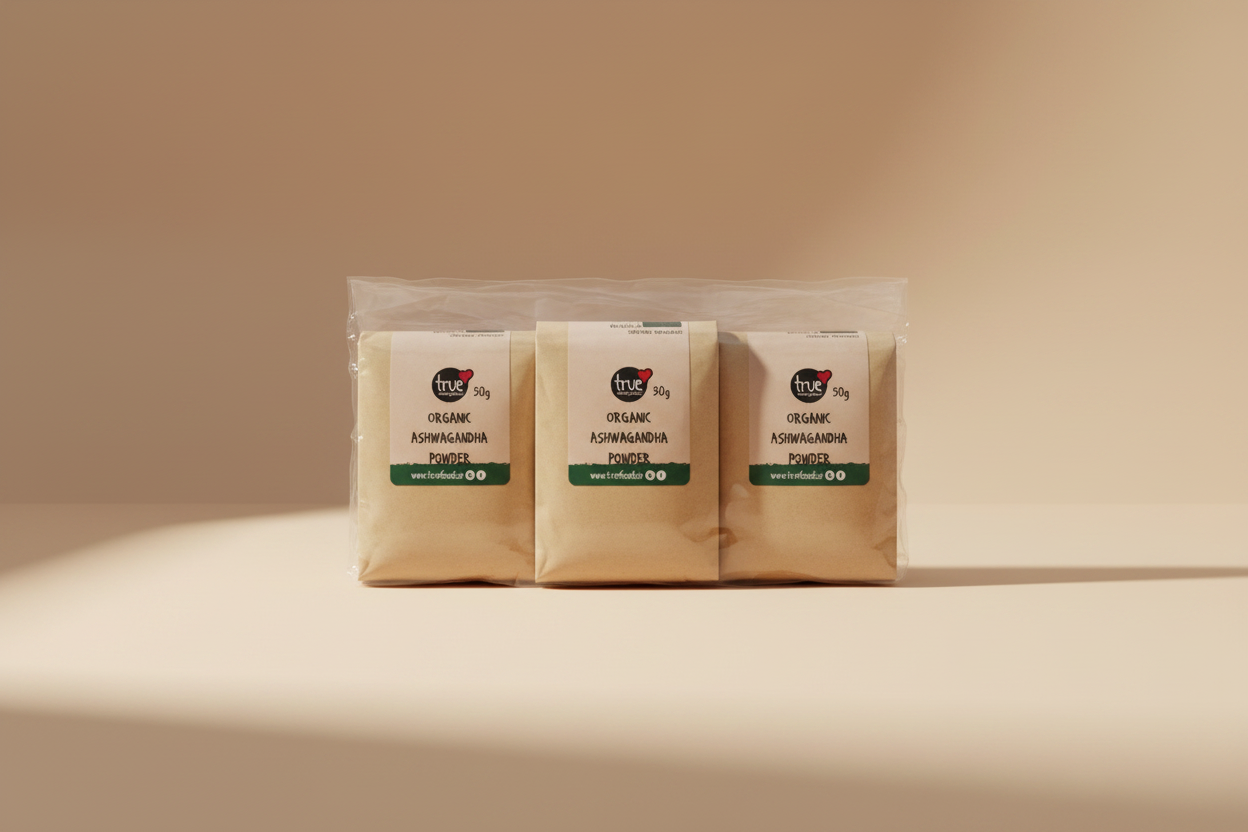 Three small brown kraft paper pouches of True Organic Ashwagandha Powder, sealed together in a clear plastic bag, photographed on a gray surface.