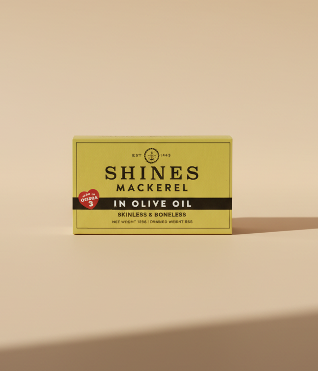 A box of Shines Mackerel In Olive Oil skinless and boneless net weight 150g, shown on a light purple background with other partially visible boxes.