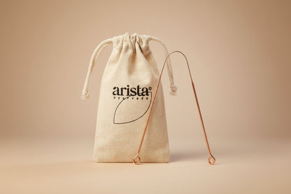 Copper hook with 'arista ayurveda' logo on a beige drawstring bag
