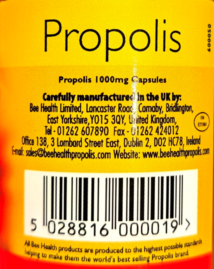 Close-up of a yellow/orange product label for Bee Health Propolis 1000mg Capsules, showing the word 'Propolis' at the top, manufacturer contact details, a barcode, and product branding text.