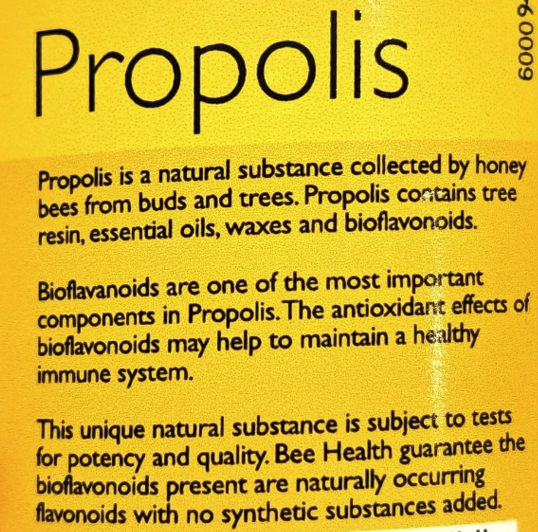 A close-up of a yellow product label with the word 'Propolis' in large black text and several paragraphs of smaller black text describing its natural components and benefits.