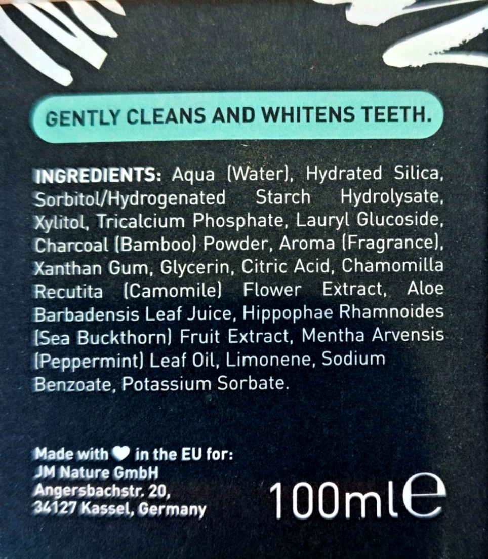 Close-up of the back of a dark toothpaste or dental care tube showing the ingredients list in white text on a black background, with a teal banner at the top reading 'GENTLY CLEANS AND WHITENST TEETH.'.