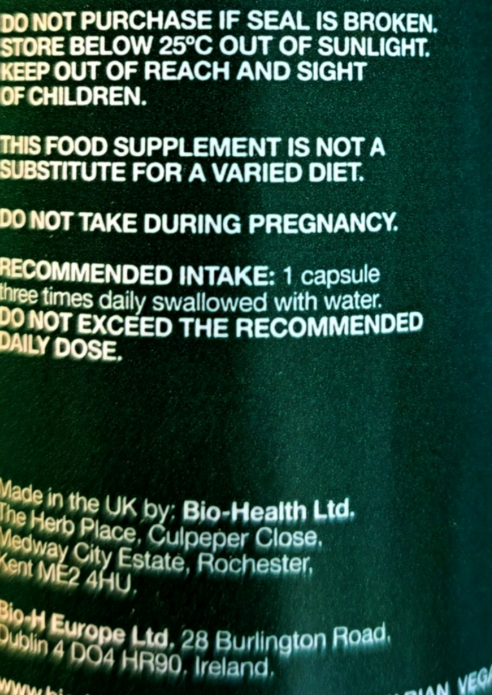 Close-up of a dark green supplement bottle label with white text showing warning and usage information.