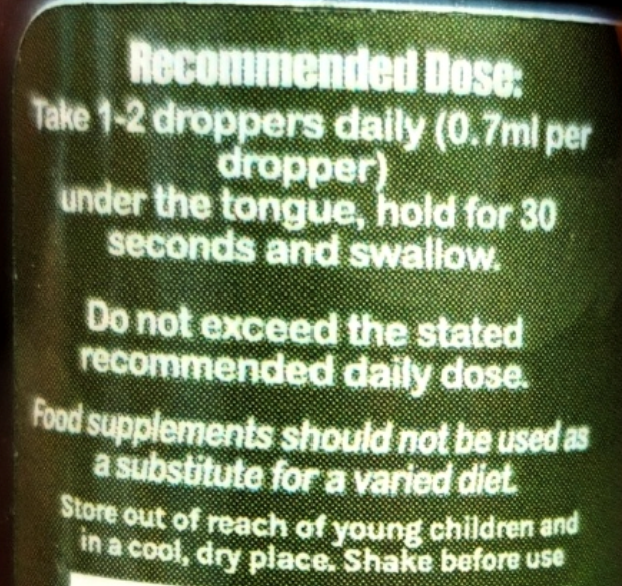 Close-up of a dark label with white text reading 'Recommended Dose:' and instructions about using a dropper daily for a food supplement.