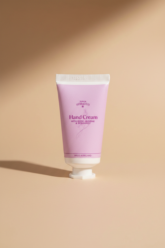 A squeeze tube of Dublin Herbalists Hand Cream with Rose, Jasmine & Bergamot, featuring a light pink body and white cap, on a clean white background.