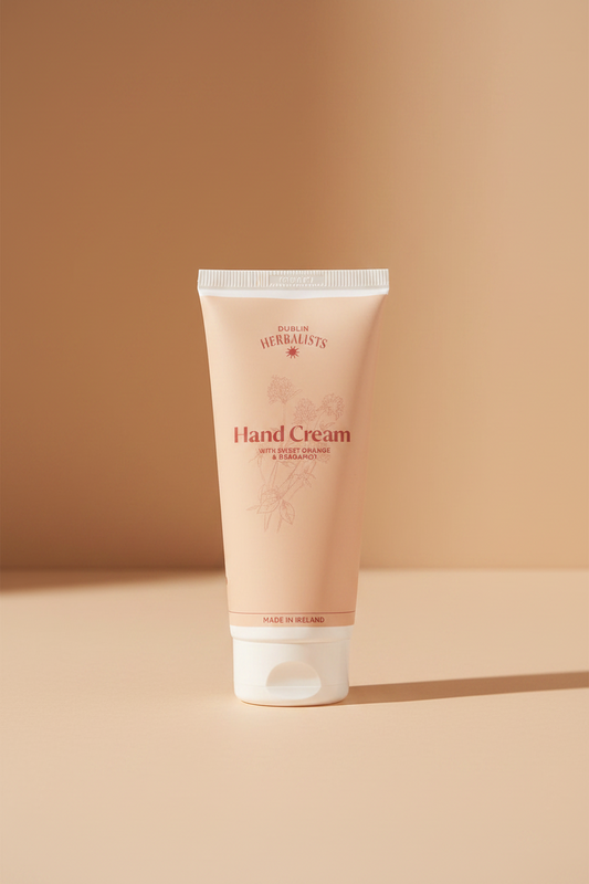 A squeeze tube of Dublin Herbalists Hand Cream with Sweet Orange and Bergamot, featuring a pale peach-pink body with white cap and base, on a white background.