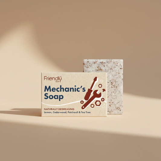 A bar of Friendly Soap Mechanic's Soap with its cardboard packaging, featuring a speckled beige soap bar and a beige label with blue and red text and graphics.