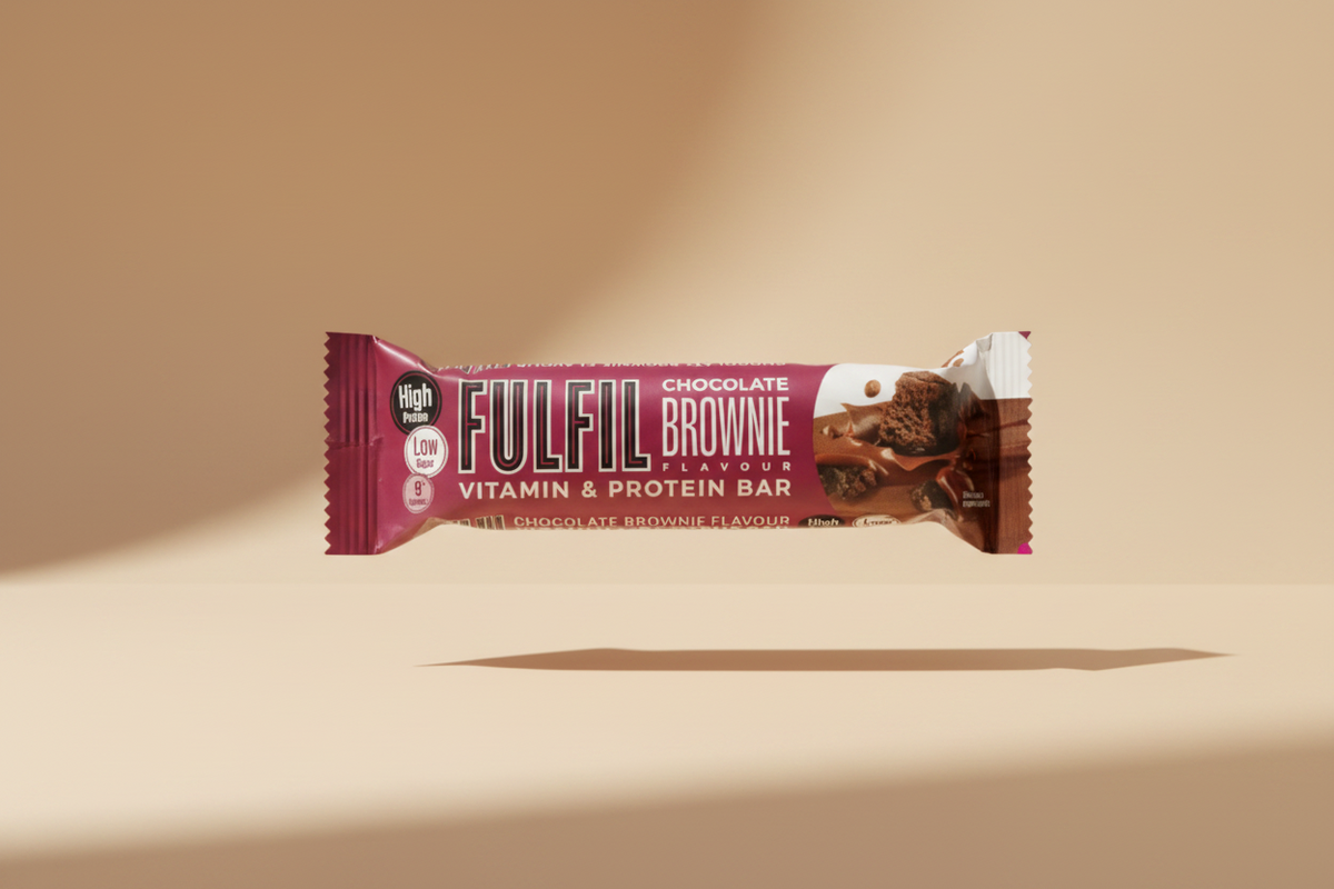 A Fulfil Chocolate Brownie Flavour Vitamin & Protein Bar wrapped in a pink and purple wrapper, held in dark gray fabric.