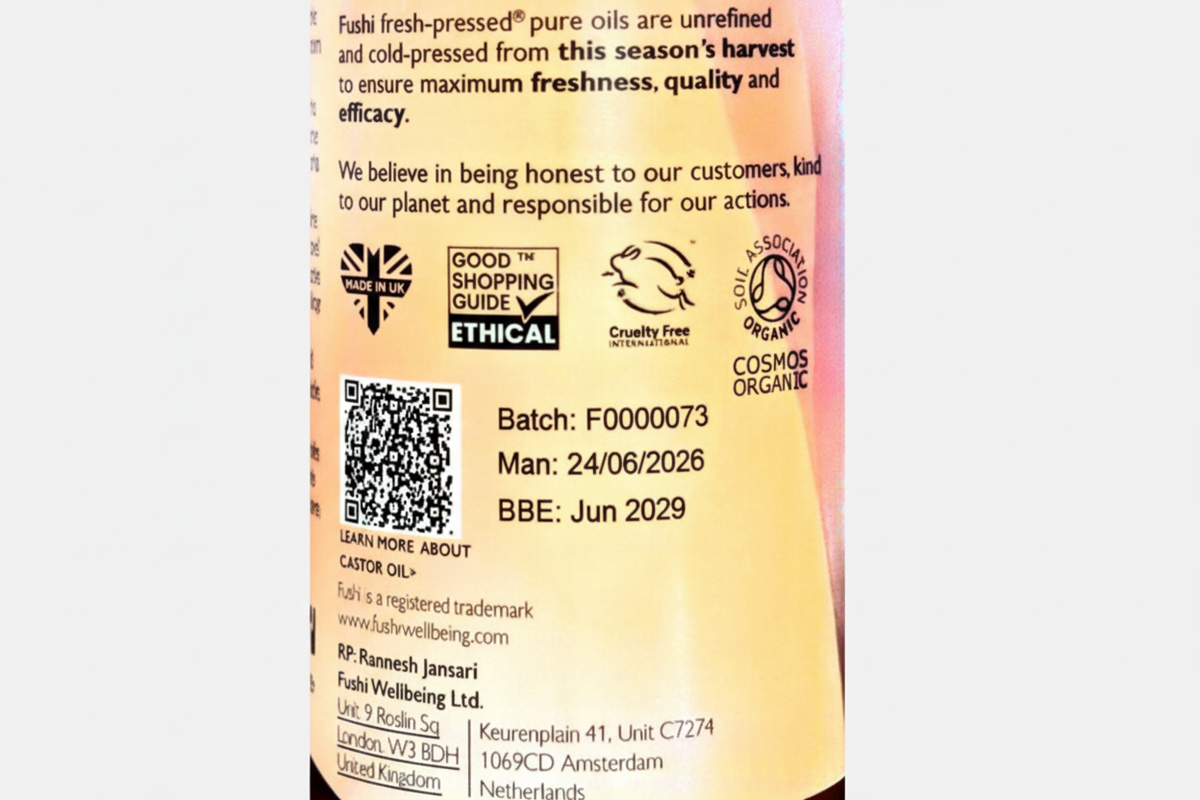 Close-up of a product label showing text about Fushi fresh-pressed pure oils, ethical certification logos, a QR code, and manufacturing details on a pinkish background.