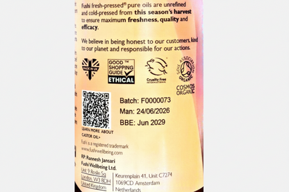 Close-up of a product label showing text about Fushi fresh-pressed pure oils, ethical certification logos, a QR code, and manufacturing details on a pinkish background.
