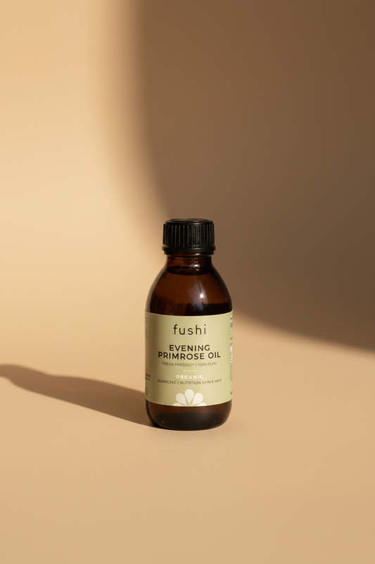 A hand holding a small dark amber bottle of Fushi Evening Primrose Oil. The bottle has a light sage green label with black text and a black screw cap.