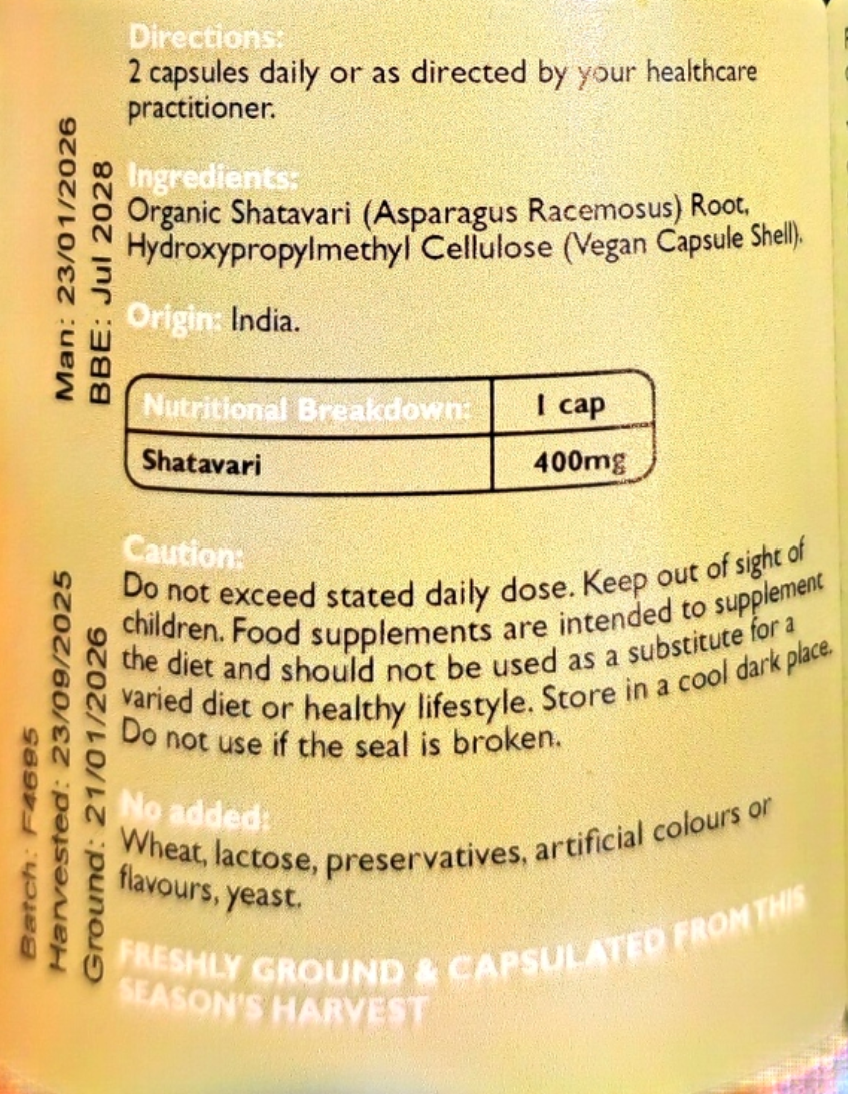 Close-up of a supplement package label showing text for Shatavi capsules, including directions, ingredients, nutritional breakdown (1 cap, 400mg), caution, and harvest details on a beige background.