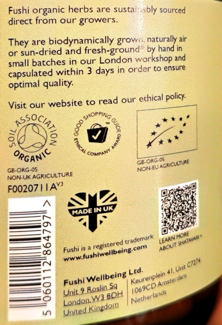 Back of a Fushi Wellbeing product package showing text about organic sourcing, ethical claims, a barcode, address, website, and a QR code on a beige background.