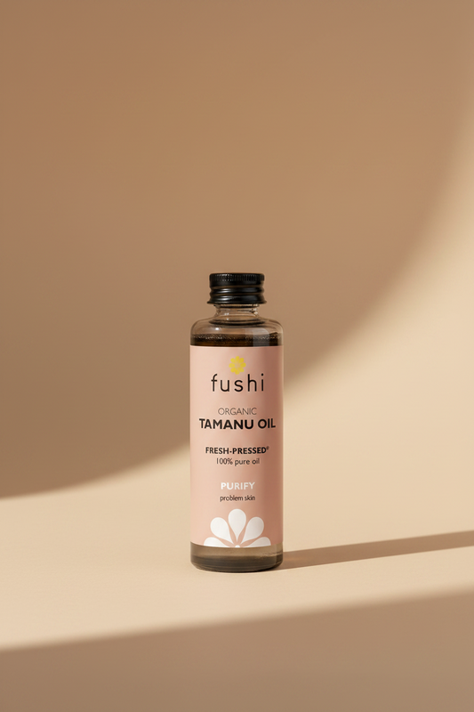 A bottle of Fushi Organic Tamanu Oil, fresh-ppressed, 100% pure oil, with a black cap and a dusty pink label on a white background.