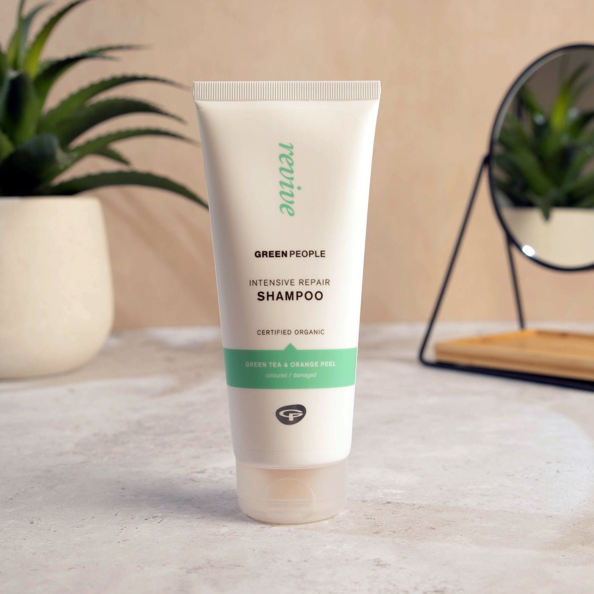 Green People Intensive Repair Shampoo 200ml beside a plant and mirror on a bathroom counter