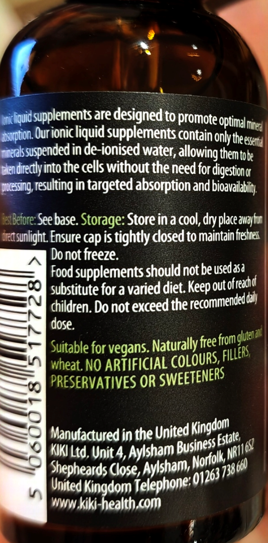 Close-up of the back label of an amber brown bottle of liquid supplements, showing product details, warnings, and manufacturer information in black, white, and green text.