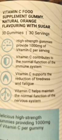 Close-up of a supplement gummy package showing text for Vitamin C food supplement gummy in natural orange flavouring with sugar, with icons describing benefits of Vitamin C.