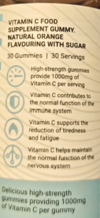 A close-up of a Vitamin C food supplement gummy package showing text and icons on a light blue background.
