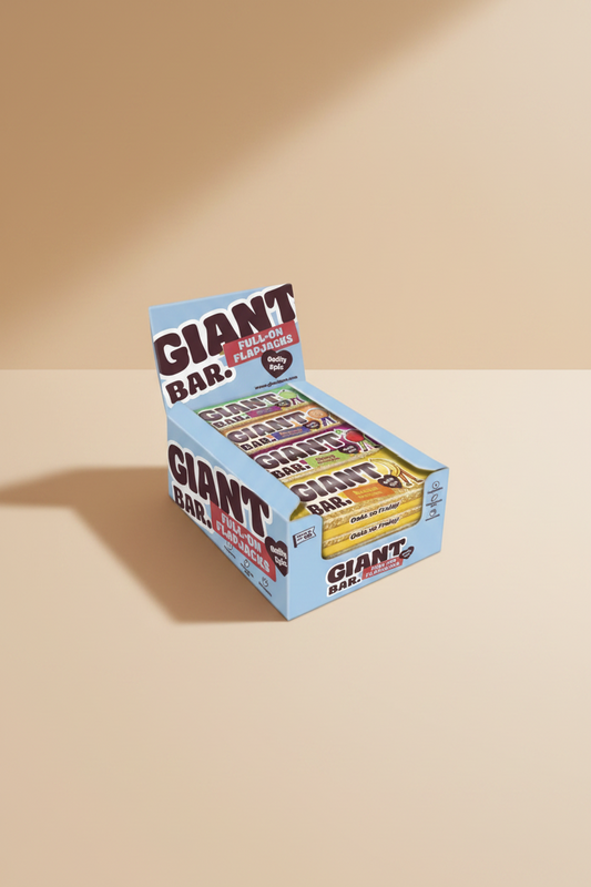 A display box of Giant Bar full-on flapjacks, showing several individually wrapped bars inside a light blue cardboard tray with large GIANT BAR branding on a tan background.