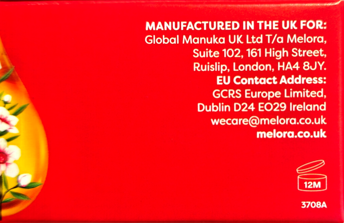 Close-up of a red product box showing white text with UK manufacturing details for Melora, plus a partial floral illustration on the left and a small 12M icon near the bottom right.