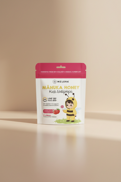 Melora Mânuka Honey Kids Lollipops in a stand-up pouch package. The packaging features a white and pink design with a cartoon bee holding a lollipop and a strawberry graphic indicating the Mânuka Honey & Strawberry flavor.