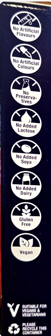 A close-up of the back of a dark blue packaged product showing a vertical list of certification and ingredient claims in white text and circular icons, including 'No Animal Based Flavours', 'No Artificial Colours', 'No Preservatives', 'No Added Lactose', 'No Added Soya', 'No Added Dairy', 'Duluth Free', 'Vegan', and 'Please Recycle This Container'.