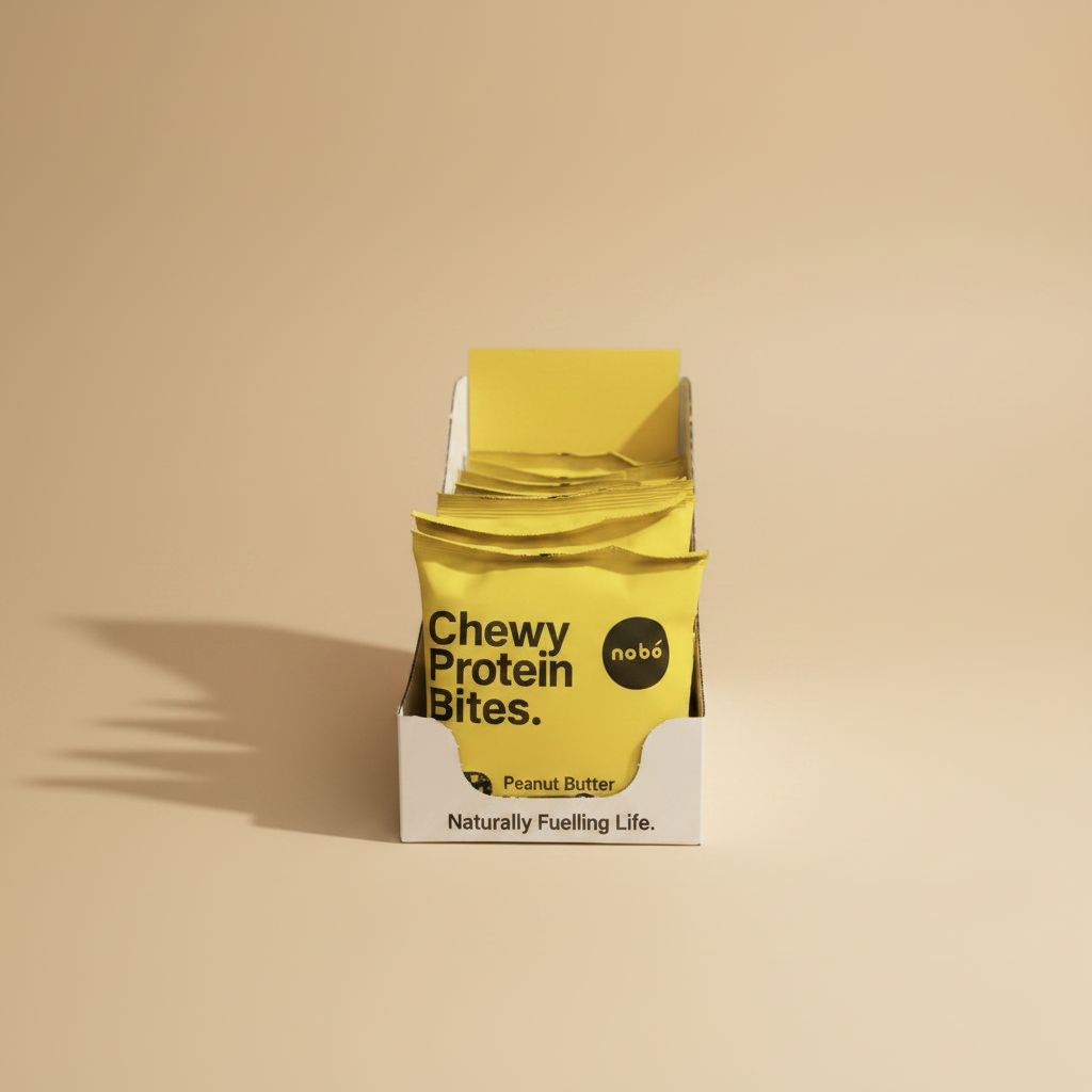 A white cardboard display box filled with bright yellow Chewy Protein Bites packets in Peanut Butter flavor. The packets feature black text and a circular black logo with the brand name 'nobl6' in white.