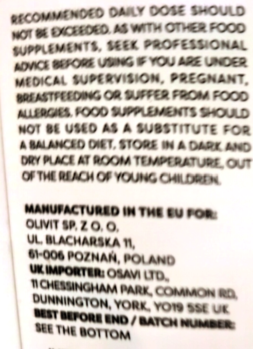 Close-up of a supplement package label showing white text on a dark background with dosage and manufacturing information.