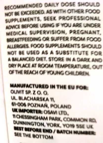 Close-up of a supplement package label showing white text on a dark background with dosage and manufacturing information.
