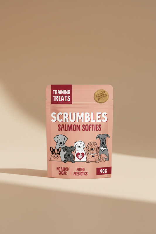 A 90g pouch of Scrumbles Salmon Softies dog training treats. The packaging is a dusty salmon-pink color with white and dark red text, featuring cartoon illustrations of various dog breeds and a single softie treat shown in the top right corner.
