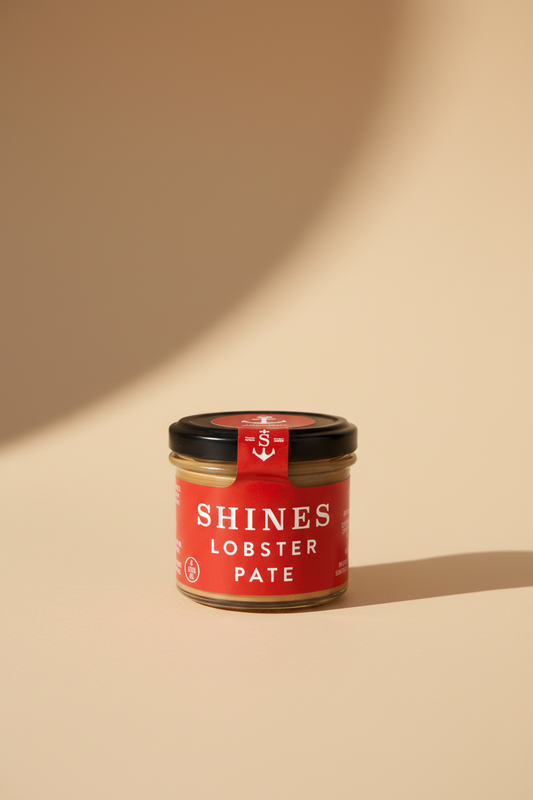 A jar of Shines Lobster Pate held in a gloved hand. The product features a bright red label with white text and a black lid sealed with a red anti-theft sticker.