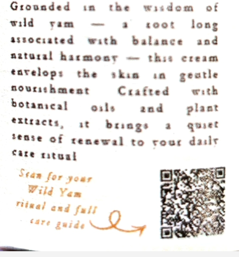 A close-up of a cream-colored product label featuring brown text describing a 'Grounded in the wisdom of wild yam' ritual, a brown arrow pointing to a QR code, and a partially visible square product package.