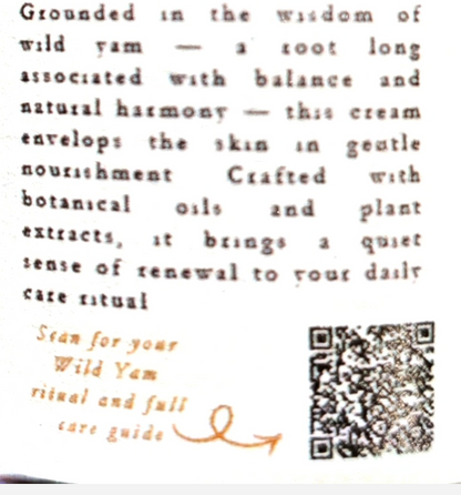 A close-up of a cream-colored product label featuring brown text describing a 'Grounded in the wisdom of wild yam' ritual, a brown arrow pointing to a QR code, and a partially visible square product package.