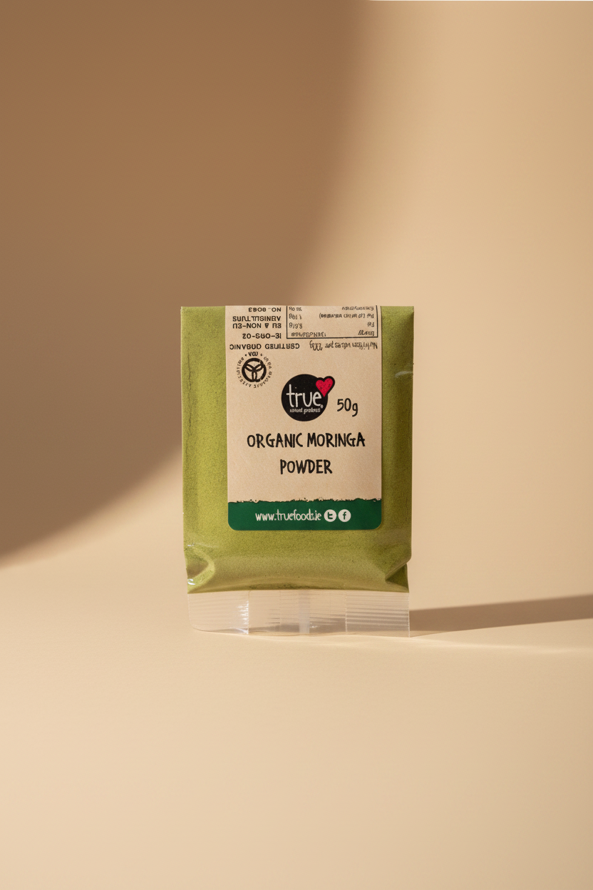 A 50g packet of True Organic Moringa Powder, showing the green powder through a clear plastic wrapper with a beige and green label, placed on a stainless steel surface.