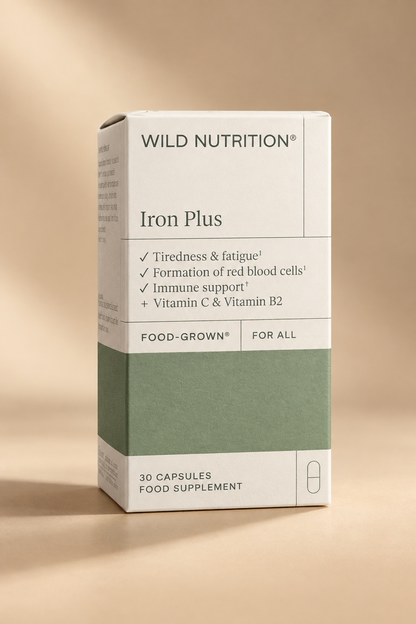 A hand holding a box of Wild Nutrition Iron Plus food supplement. The packaging is white with a sage green lower section and black text.