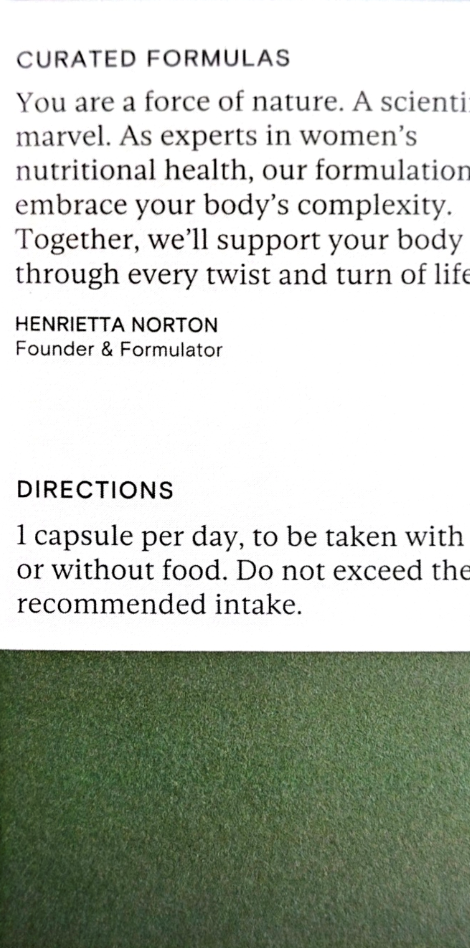 A close-up of a white printed card or label with black text, including the headline 'CURATED FORMULAS,' a quote attributed to Henrietta Norton, and dosage instructions. The lower portion shows a green textured surface.