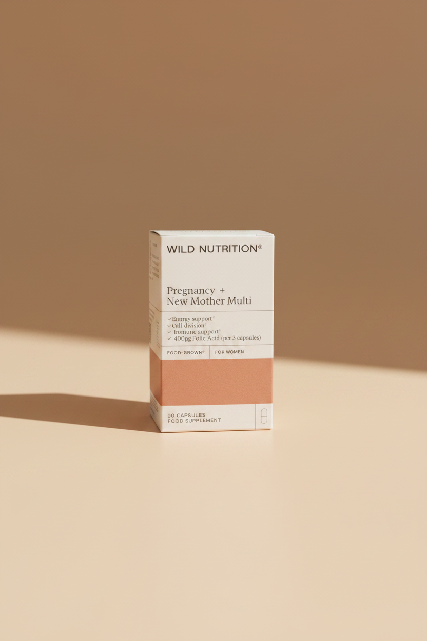 A box of Wild Nutrition Pregnancy + New Mother Multi dietary supplement, shown lying on a dark fabric surface. The packaging is white with a peach-colored side panel and black text.