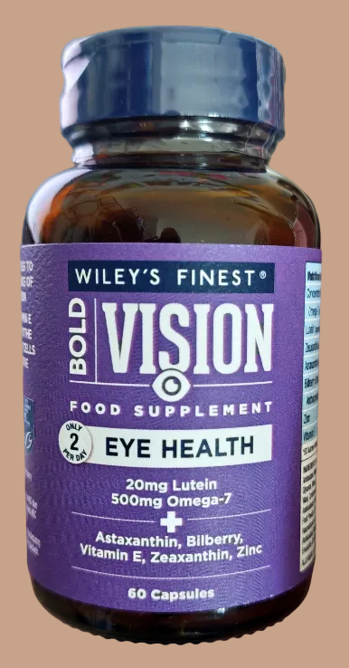 A hand holding a bottle of Wiley's Finest Bold Vision Eye Health food supplement. The bottle is amber brown with a dark purple label and a dark blue cap.