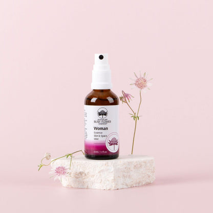 Woman Essence Skin and Space Mist 50ml displayed with flowers on a pink background